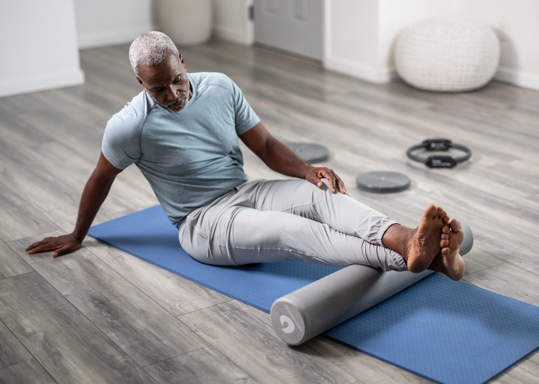 Man on mat stretching legs over a Balanced Body foam roller