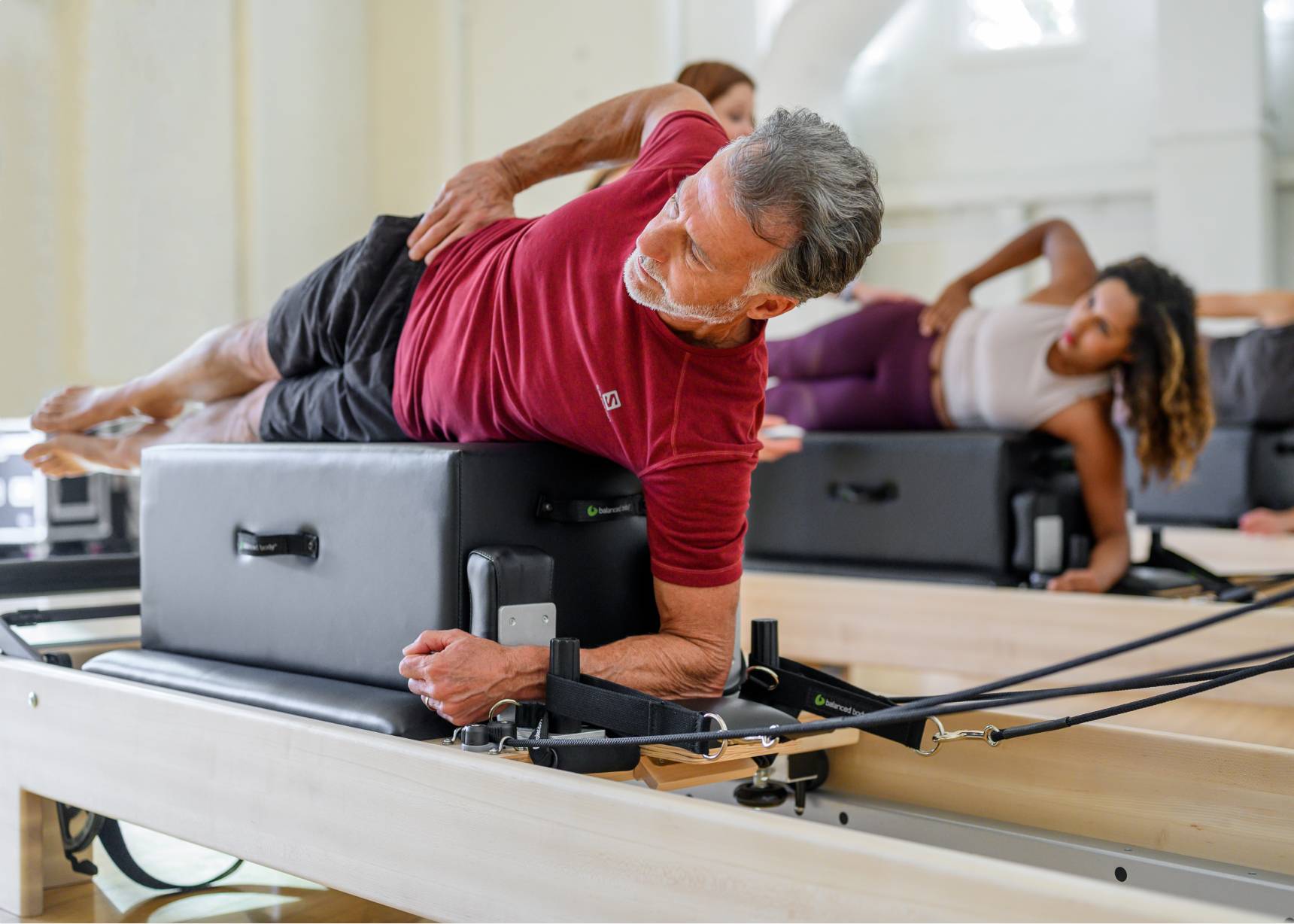 Students in a Pilates class laying in a side plank position on a sitting box on top of a reformer