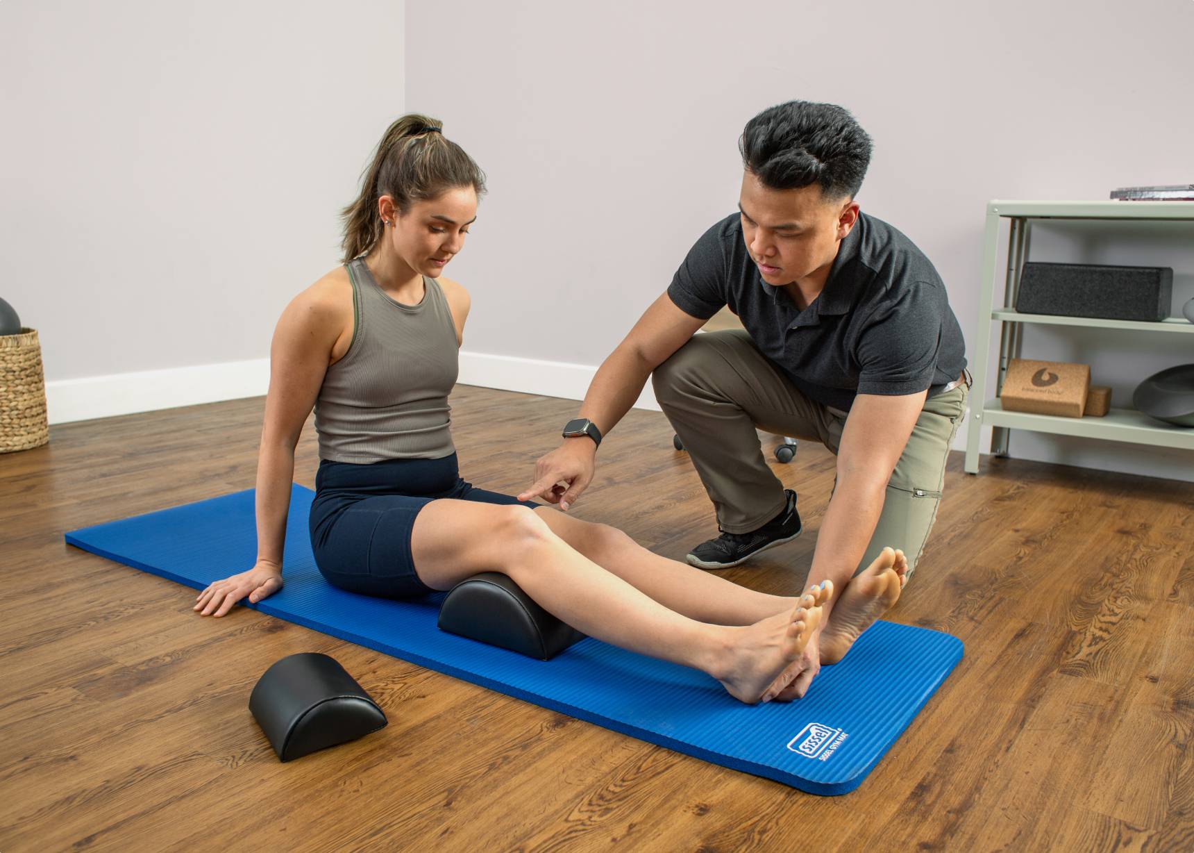 Physical therapist pointing out knee positioning while therapist does mat Pilates exercise