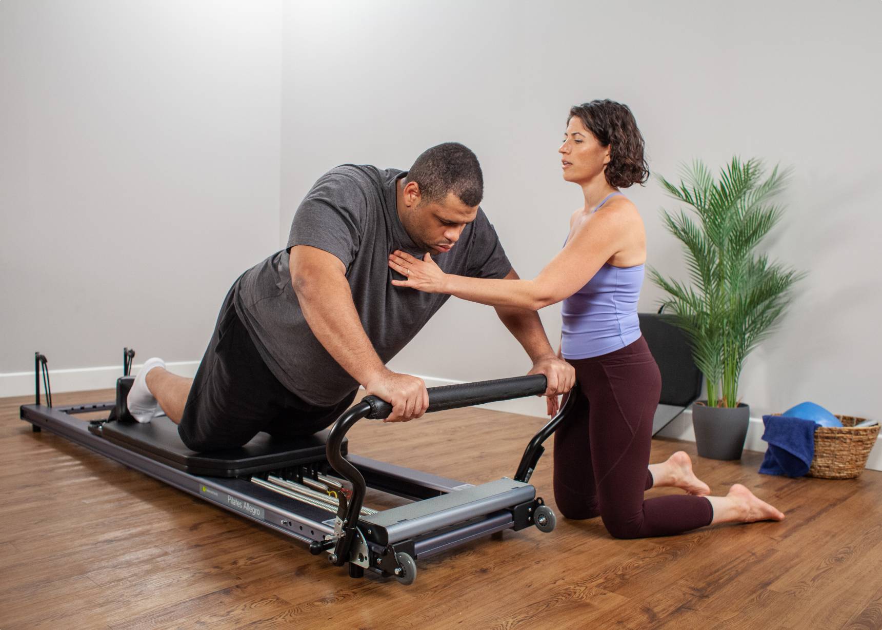 Pilates instructor guides a large male athlete as he leans forward against the footbar on the Allegro Stretch Reformer